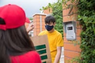 pexels-photo-8931654-8931654-1 Masked man receiving a delivery from a courier outdoors. Safety measures in place.