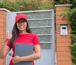 pexels-photo-8931665-8931665-1 Smiling female courier giving a thumbs up in front of a residential gate, holding a clipboard.